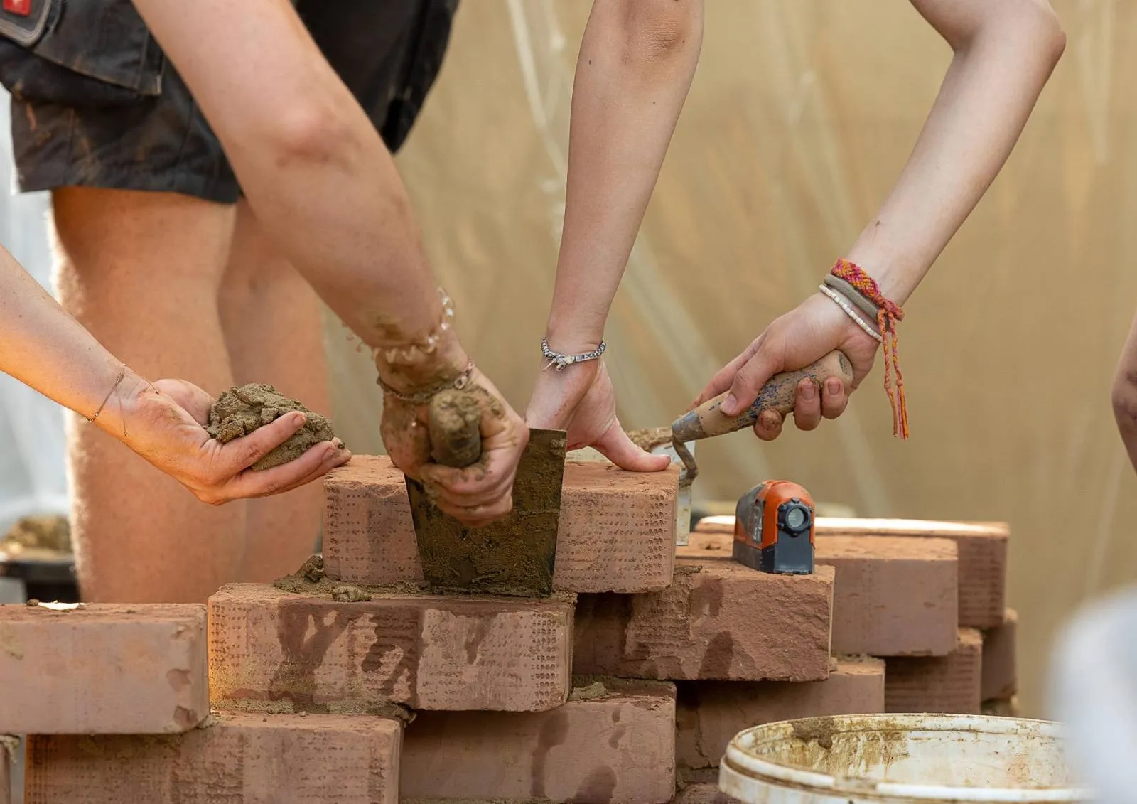 A stack of clay bricks being built. Some hands can be seen working.